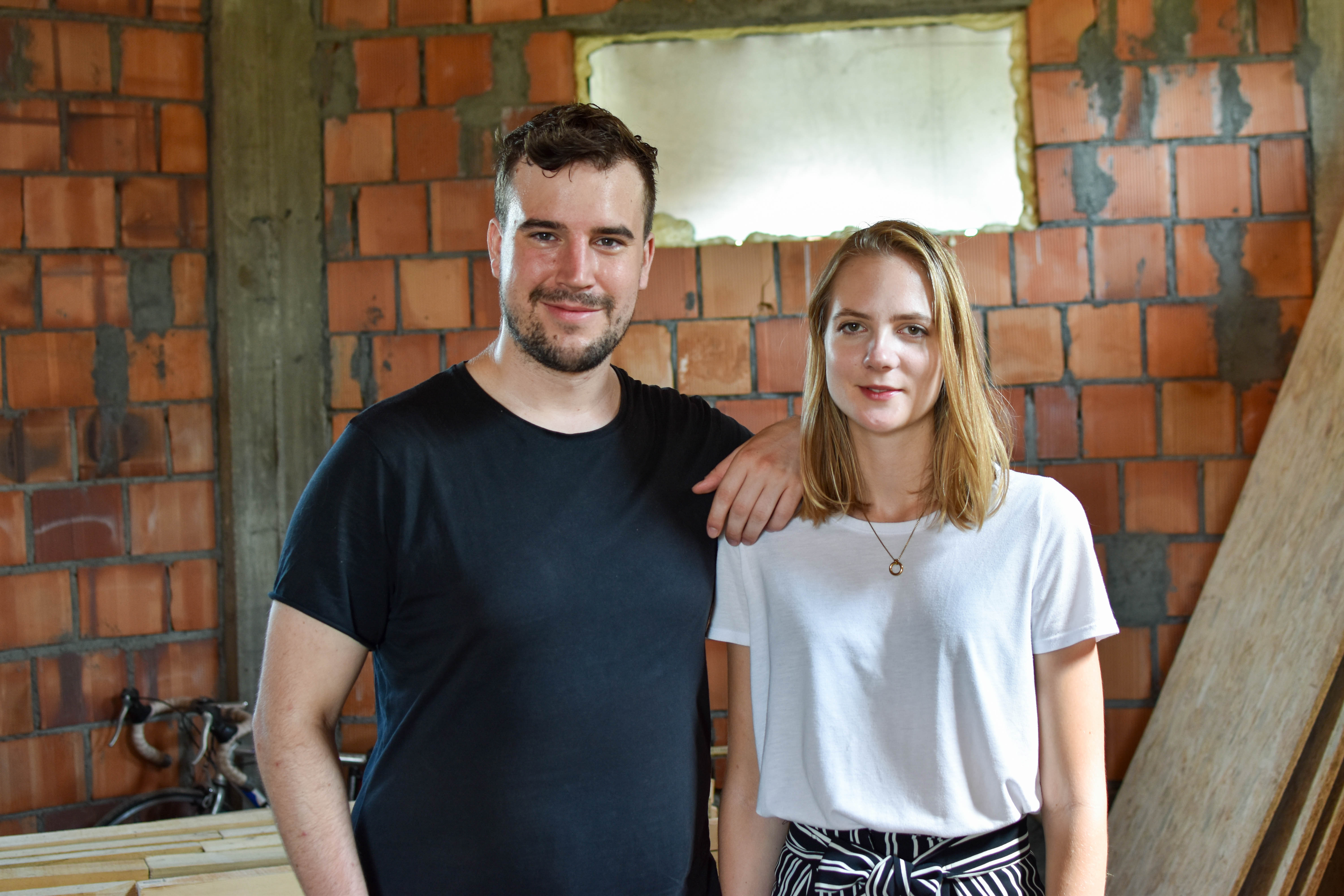 Two smiling people pose for a photograph in front of a brick wall.